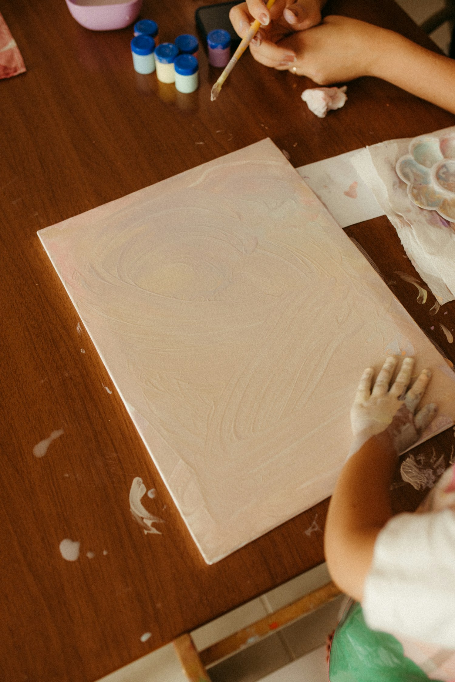 A young child painting with an adult nearby